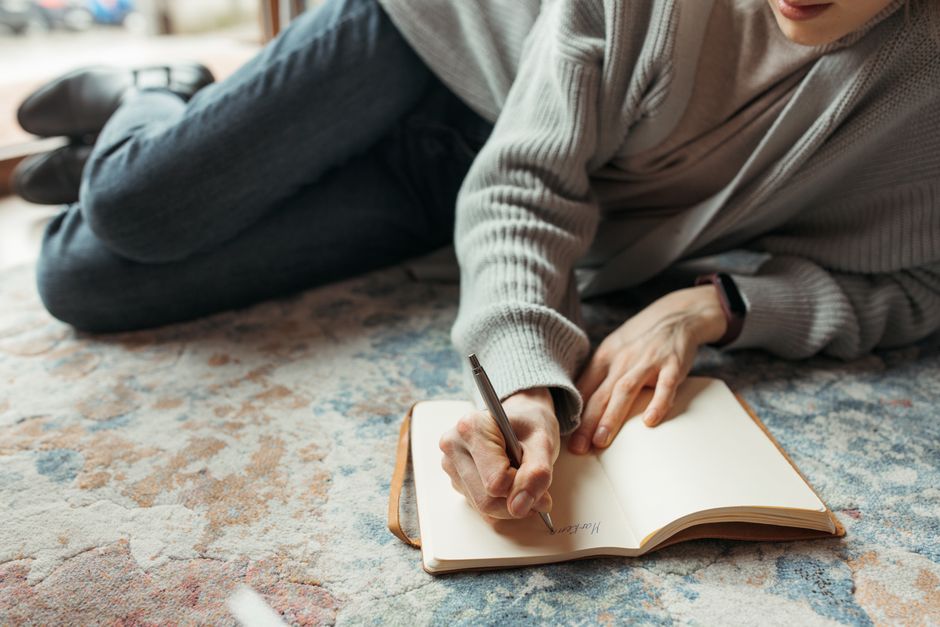 A person sitting at a clean desk, writing in a notebook with a pen, surrounded by a planner and a cup of tea, indicating organization.