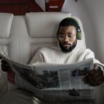 Person wearing over-ear noise-cancelling headphones, relaxing in an airplane seat, looking calm amidst other passengers.