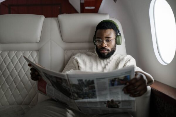 Person wearing over-ear noise-cancelling headphones, relaxing in an airplane seat, looking calm amidst other passengers.