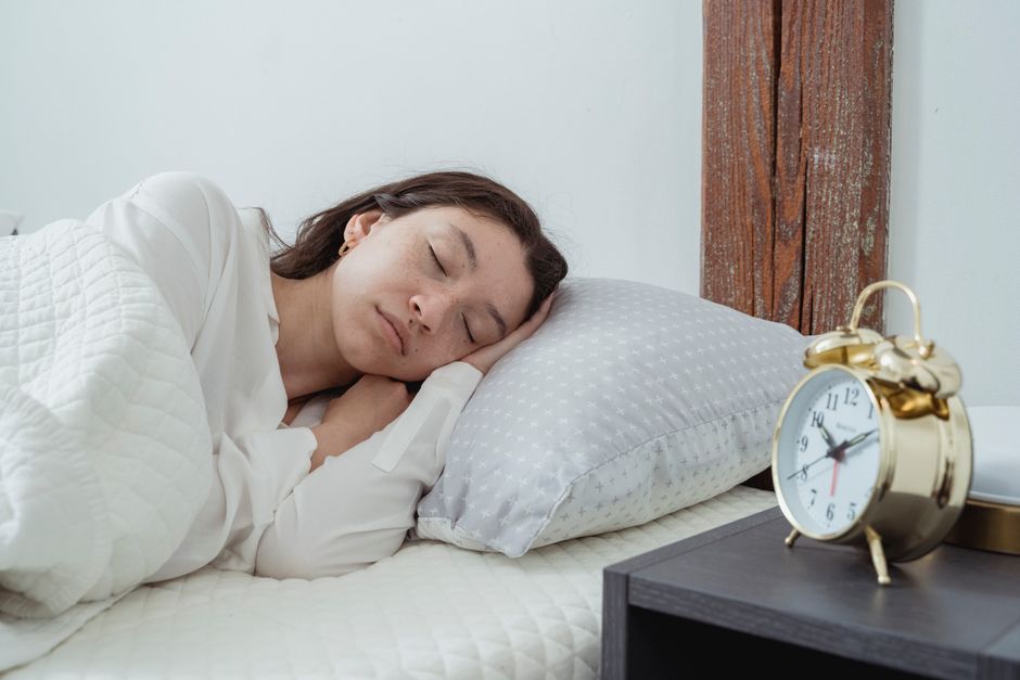 A person lying in bed, illuminated by a smartphone screen, looking tiredly at a digital clock showing late hours, symbolizing digital distraction before sleep.