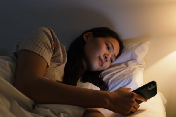 A person's hand holding a smartphone displaying a sleep tracking app's detailed graphs and data, with a blurred bedroom in the background, illustrating data interpretation.
