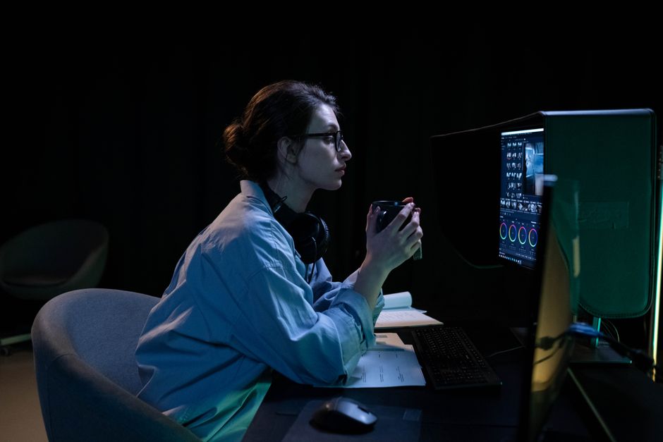 A person sitting at a desk, looking intently at two computer monitors, one displaying work documents and the other a game, illustrating the dual purpose.