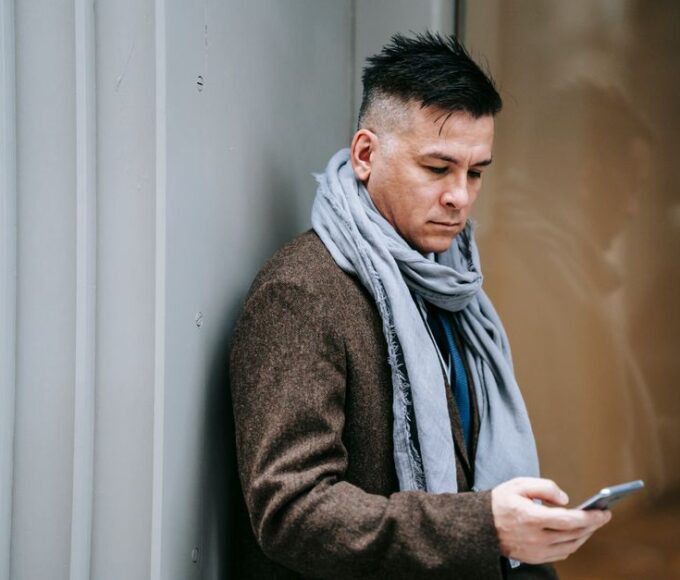 A person with a confused expression holding a smartphone, with a blurred background showing various digital icons, representing online confusion.
