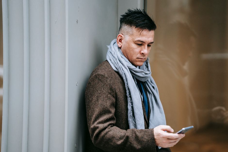 A person with a confused expression holding a smartphone, with a blurred background showing various digital icons, representing online confusion.