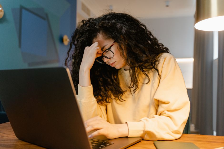 A person with head in hands at a cluttered desk, looking overwhelmed and stressed after a long work period.