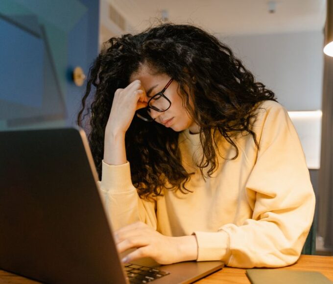 A person with glasses rubbing their eyes in front of a laptop, looking tired and overwhelmed by digital screens.