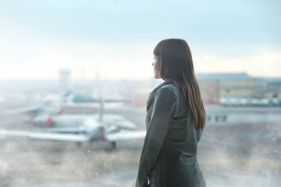A remote worker looking visibly tired and stressed while waiting in a busy airport lounge, surrounded by luggage.