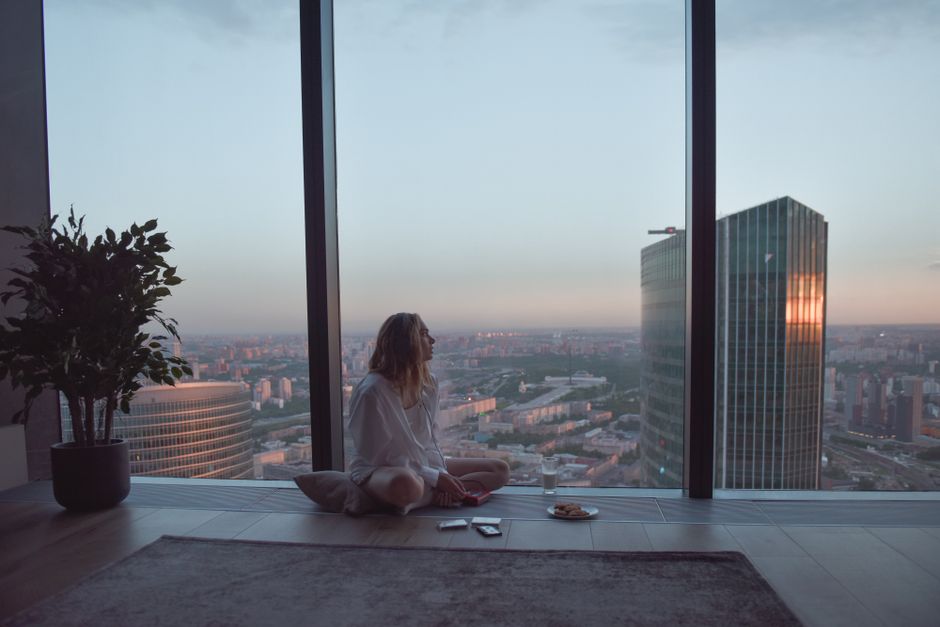 A person meditating calmly in a sunlit city apartment, overlooking urban buildings, embodying a slow morning routine.
