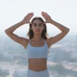 A person in activewear sits in a peaceful meditation pose on a rooftop overlooking a vibrant cityscape at sunset, symbolizing mental rest amidst a busy urban environment.