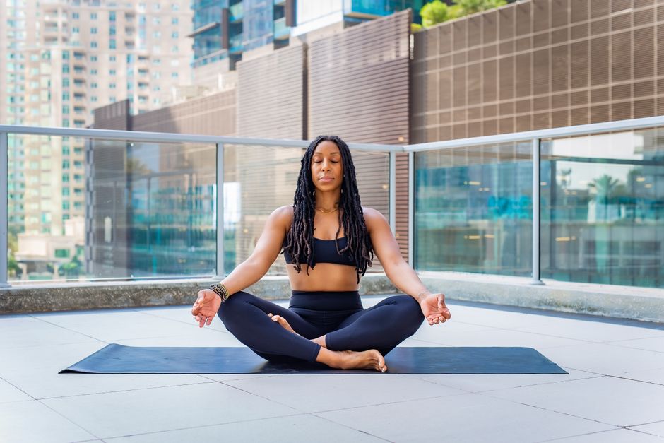 A person sitting peacefully on a small city balcony, looking out at an urban skyline during sunrise, with hands gently folded, representing a mindful start to the day.