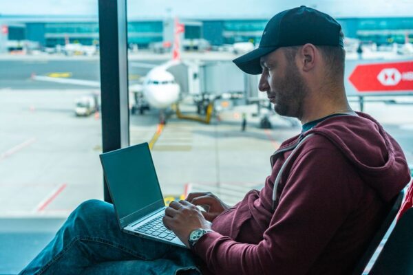 A person using a laptop with world map overlay in a modern airport lounge, depicting international work and travel.
