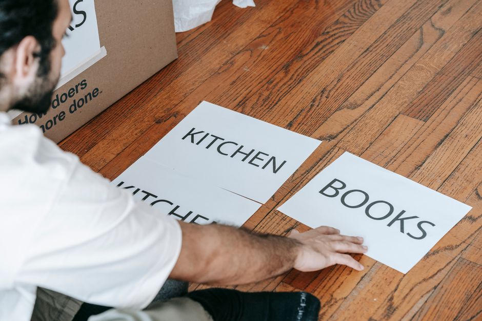 Close-up of hands writing 'Kitchen - Fragile' on a cardboard moving box with a marker.