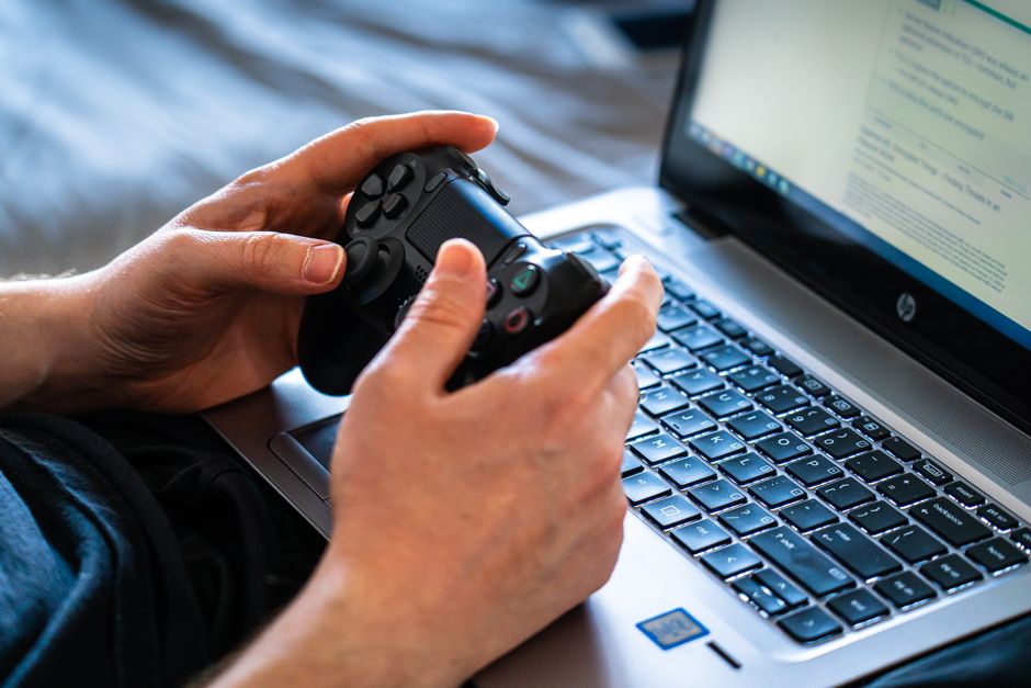A person's hands on a keyboard, with a modern city-building game displayed on a laptop screen, showing roads and buildings.