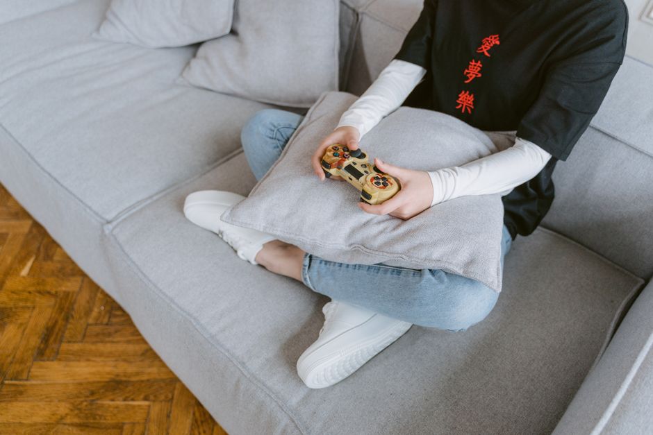 A person comfortably playing a cozy farming simulation game on a console at home, surrounded by soft lighting, illustrating relaxation after work.