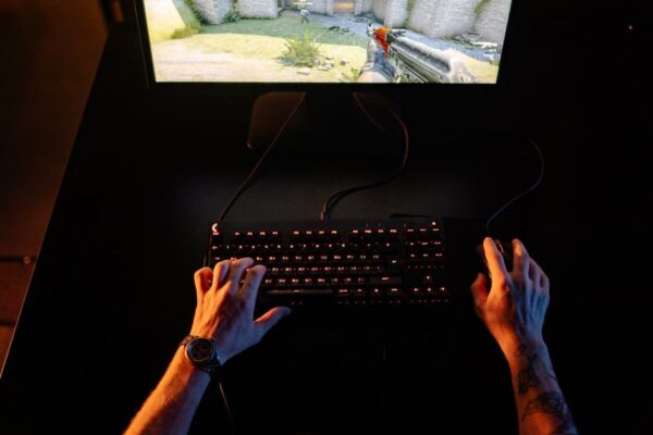 A close-up shot of hands on a keyboard and mouse, with a complex turn-based strategy game displayed on a computer monitor in the background.