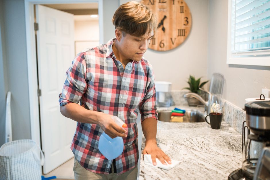 A close-up of hands quickly wiping down a clean kitchen counter with a spray bottle and microfibre cloth, demonstrating a simple, quick cleaning task.