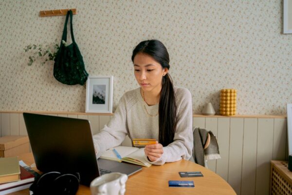 A person with a laptop and credit cards, researching options at a desk.