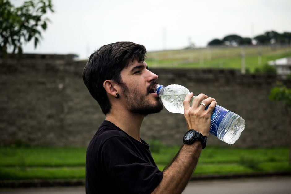 Person sipping from a reusable water bottle during a hot summer day, with sweat on their brow.