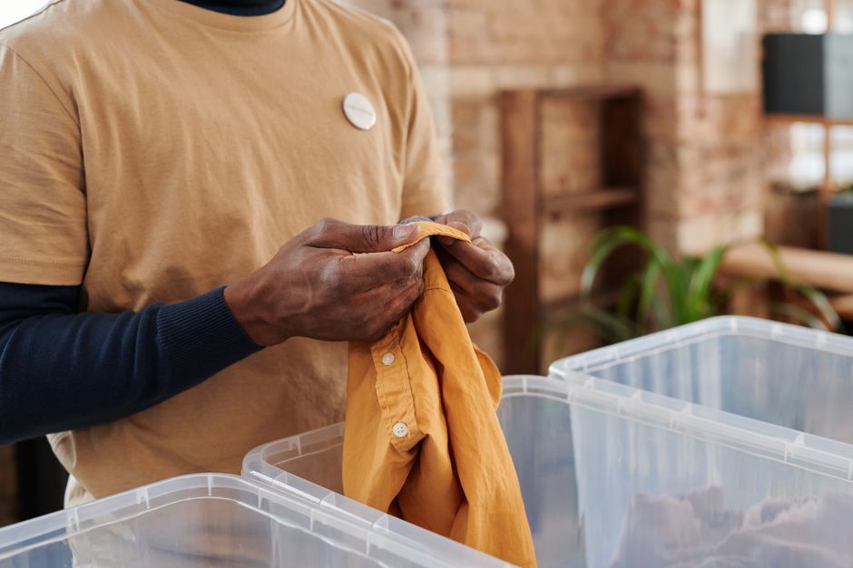 A person's hands sorting through a rack of clothes, making decisions about what to keep or donate.