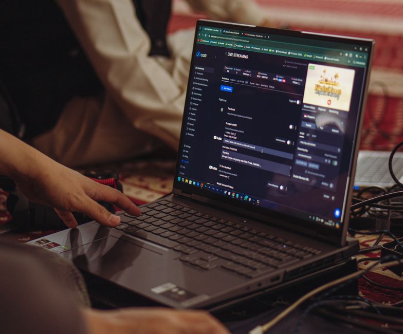 A person laughing while streaming a video game using a laptop and a smartphone as a webcam.