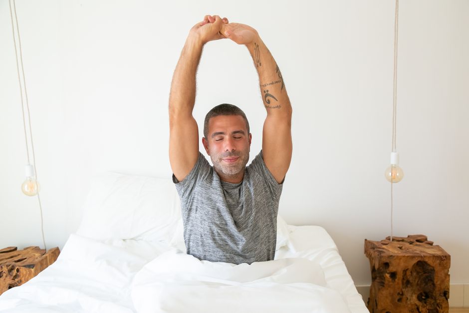 A person in comfortable clothes doing gentle stretches on a yoga mat in a sunny, modern urban apartment living room, signifying healthy morning habits without waking early.