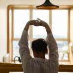 A person gently stretching in soft morning light by a window, symbolizing a calm start to the day without immediate screen time.