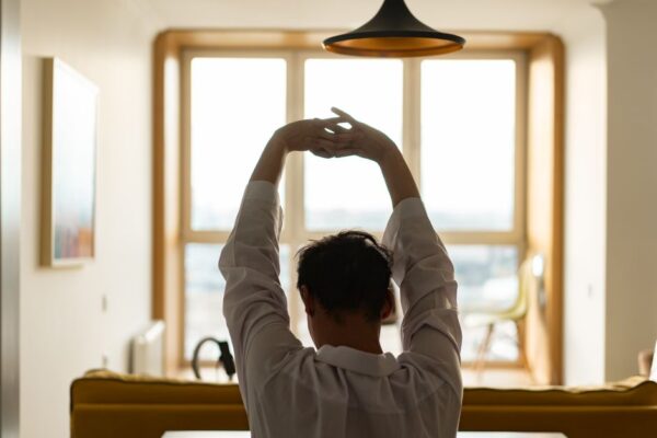 A person gently stretching in soft morning light by a window, symbolizing a calm start to the day without immediate screen time.