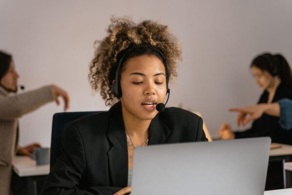 A person wearing a professional headset and microphone, gesturing while speaking on a call in a busy airport lounge, conveying the challenge of long calls during travel.