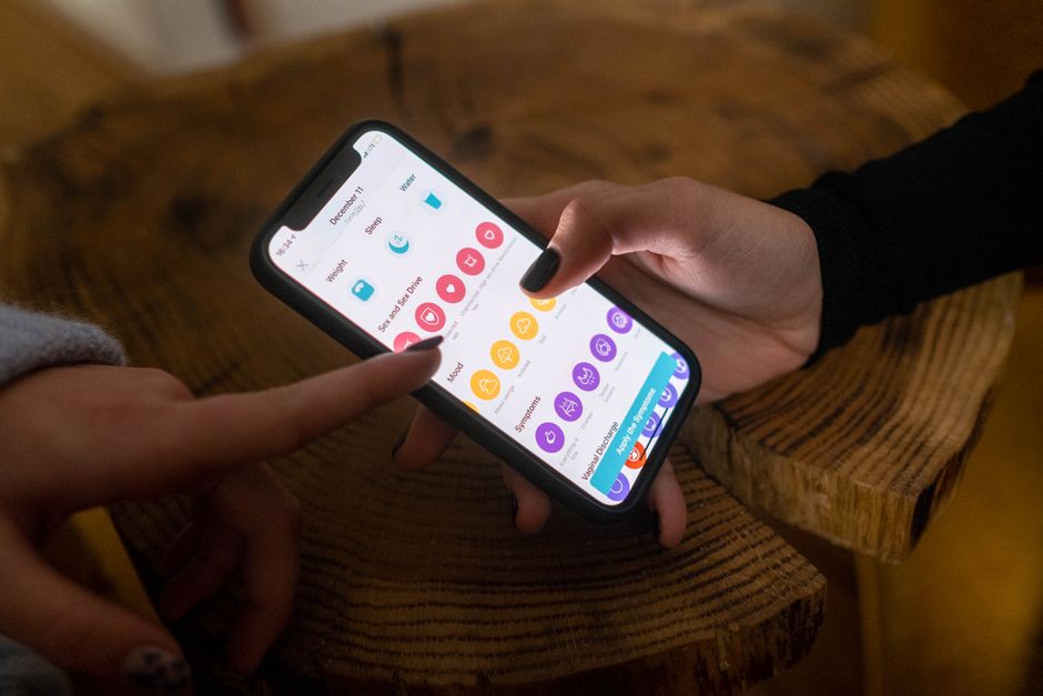 A hand holding a smartphone with a hydration tracking app open, showing water intake for the day, with a glass of water in the background.