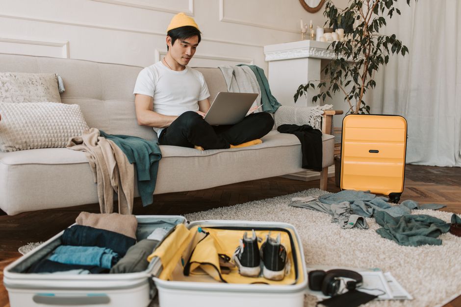 Person sitting on a bed, calmly taking items out of an open suitcase, next to a window with soft natural light.