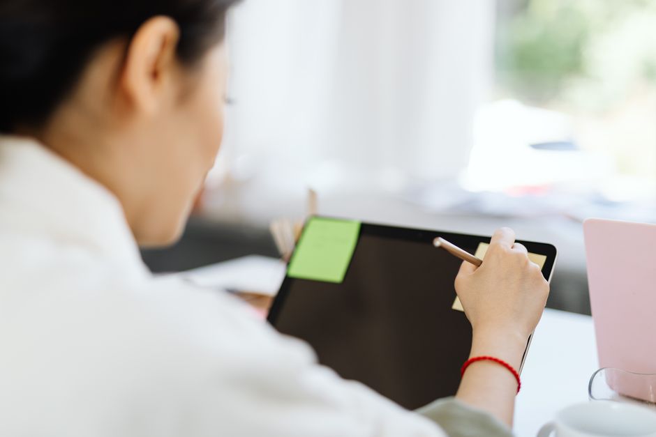 A person's hands interacting with an AI interface on a tablet, surrounded by paper notes and a coffee cup, illustrating practical use.