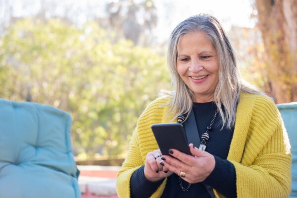 A person smiling while using a sleek, modern budget smartphone outdoors, clearly enjoying the experience.