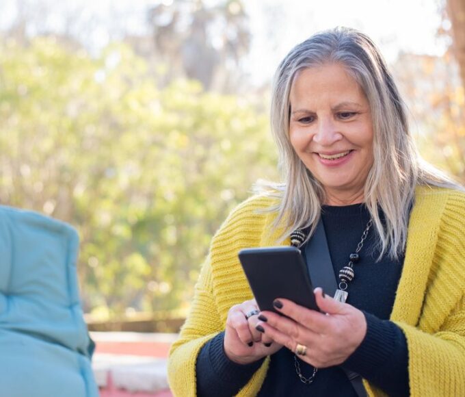A person smiling while using a sleek, modern budget smartphone outdoors, clearly enjoying the experience.