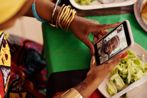 A young woman on a video call, smiling and waving at her family on screen, illustrating long-distance connection.