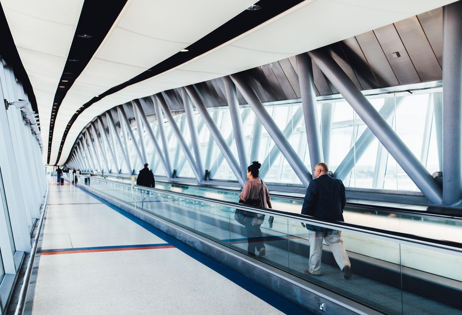 A person power-walking down a long, bright airport concourse with shops and other travelers visible in the background, illustrating purposeful movement during a layover.