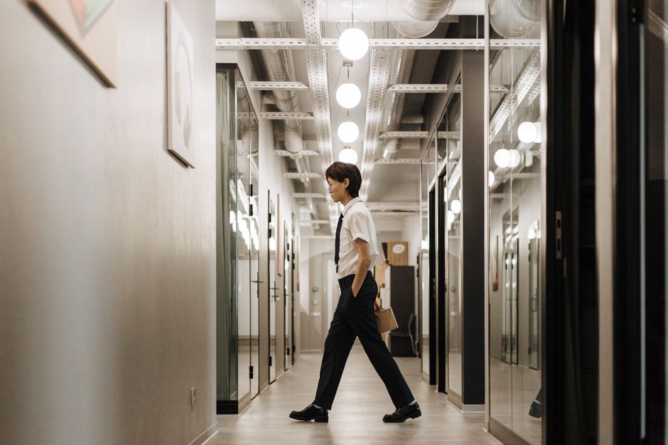 A person with noise-canceling headphones taking a brisk walk outside a modern office building during a work break.