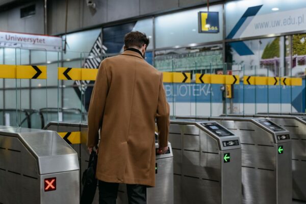 A person in business casual attire walks briskly towards a subway station entrance in an urban setting, carrying a backpack and a reusable coffee cup, embodying healthy habits public transit commute.