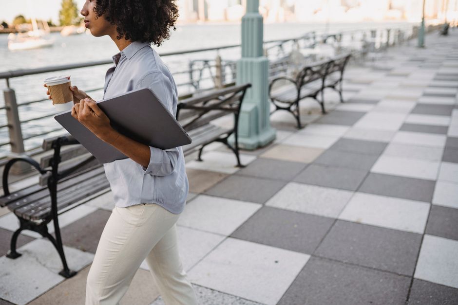 A remote worker briskly walking through a vibrant city street with a backpack and a laptop bag, looking energized.