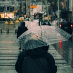 Person walking on a wet city street with an umbrella, wearing practical, dark commuter shoes.