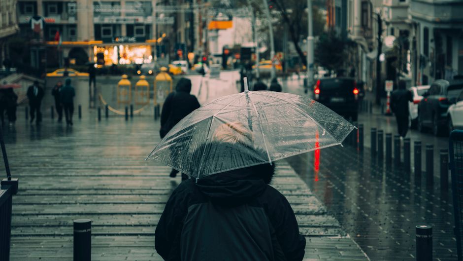 Person walking on a wet city street with an umbrella, wearing practical, dark commuter shoes.