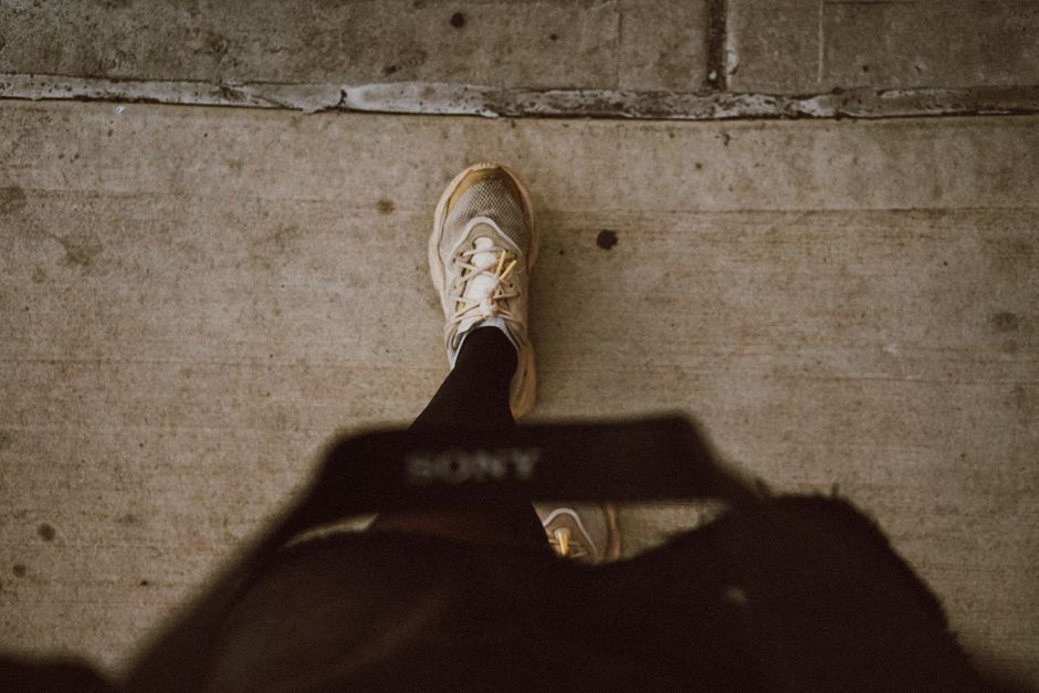 A person's legs in dark trousers and clean white leather sneakers, walking confidently on a cobblestone street in a European city.