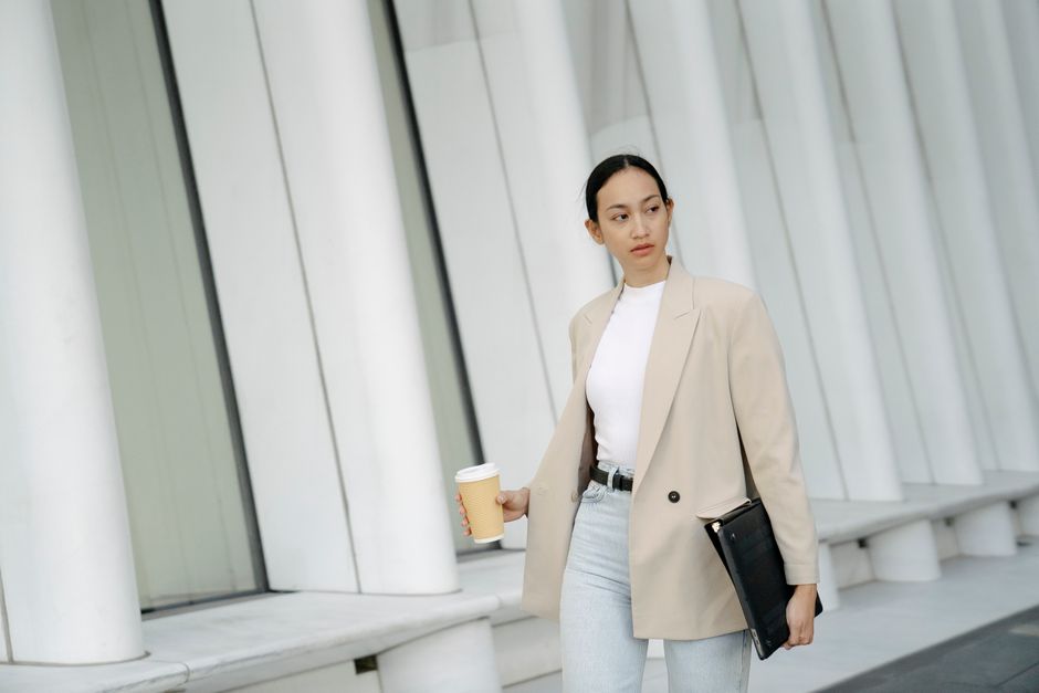 A stylish young professional walking confidently, holding a lightweight cardigan, dressed in flowy pants and a top suitable for both heat and air conditioning.