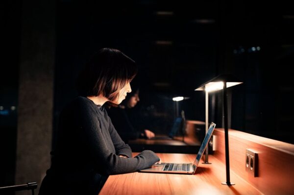 A person with headphones concentrating intently on a laptop screen, with a clean desk setup, suggesting deep work and focus in a remote environment.
