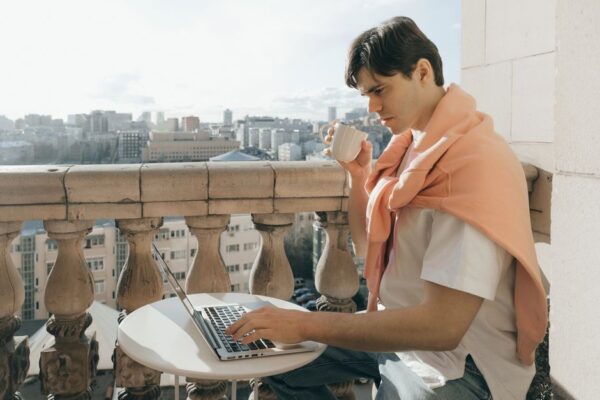 A person works on a laptop on a balcony overlooking a bustling European city, symbolizing the dream of a workcation.