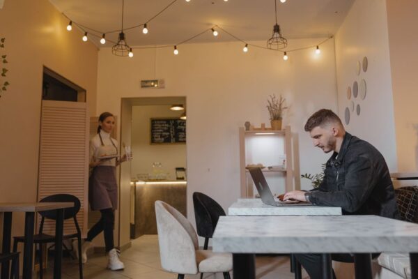 A person working remotely on a laptop at a bright, modern coffee shop, with a cup of coffee nearby.