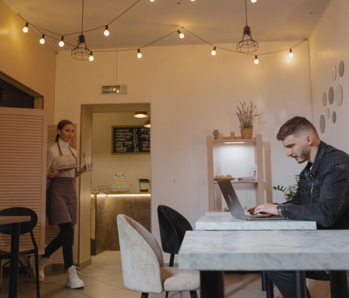 A person working remotely on a laptop at a bright, modern coffee shop, with a cup of coffee nearby.