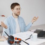 A remote worker sitting calmly at a clean desk, eyes closed in meditation, with a laptop nearby. Focuses on mental wellness in a home office.