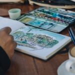 A remote worker sips coffee while sketching in a notebook, taking a creative break from work.
