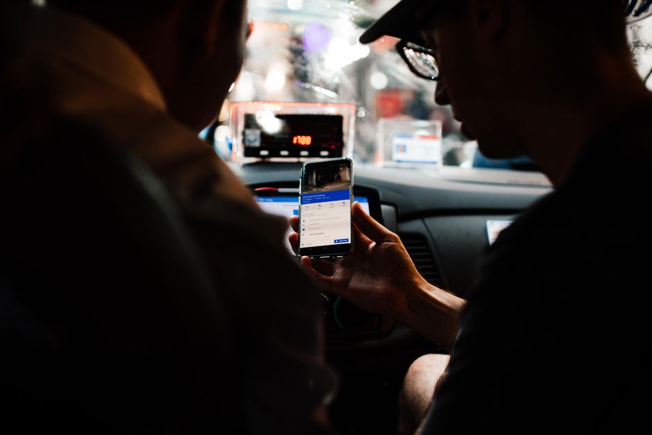A rideshare driver in a car picking up a passenger from an airport curbside at night.