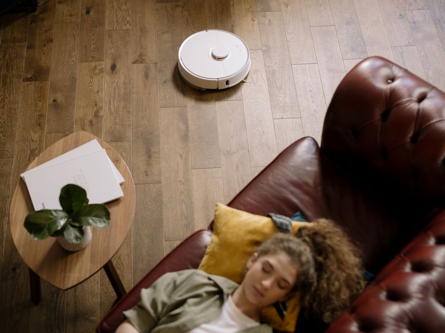 A sleek robot vacuum cleaner autonomously navigating and cleaning the floor of a tidy, compact living room.